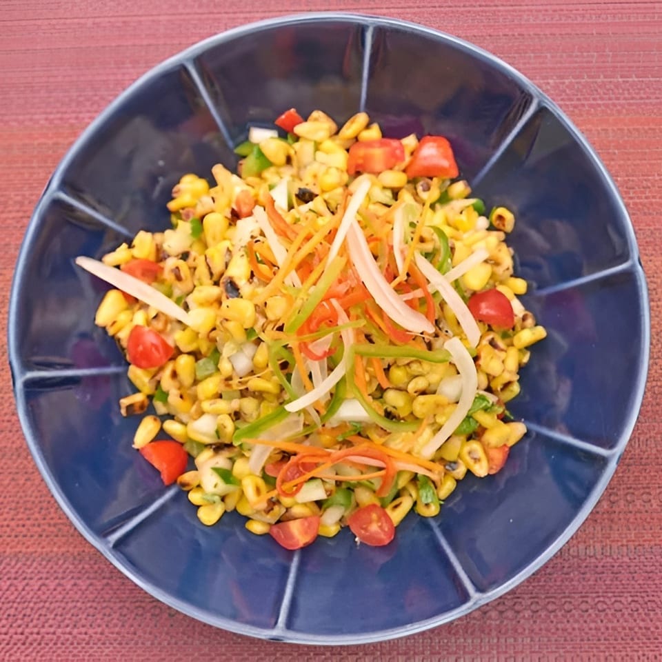 Grilled corn salad with cherry tomatoes, bell peppers, onions, and shredded carrots in a blue bowl.