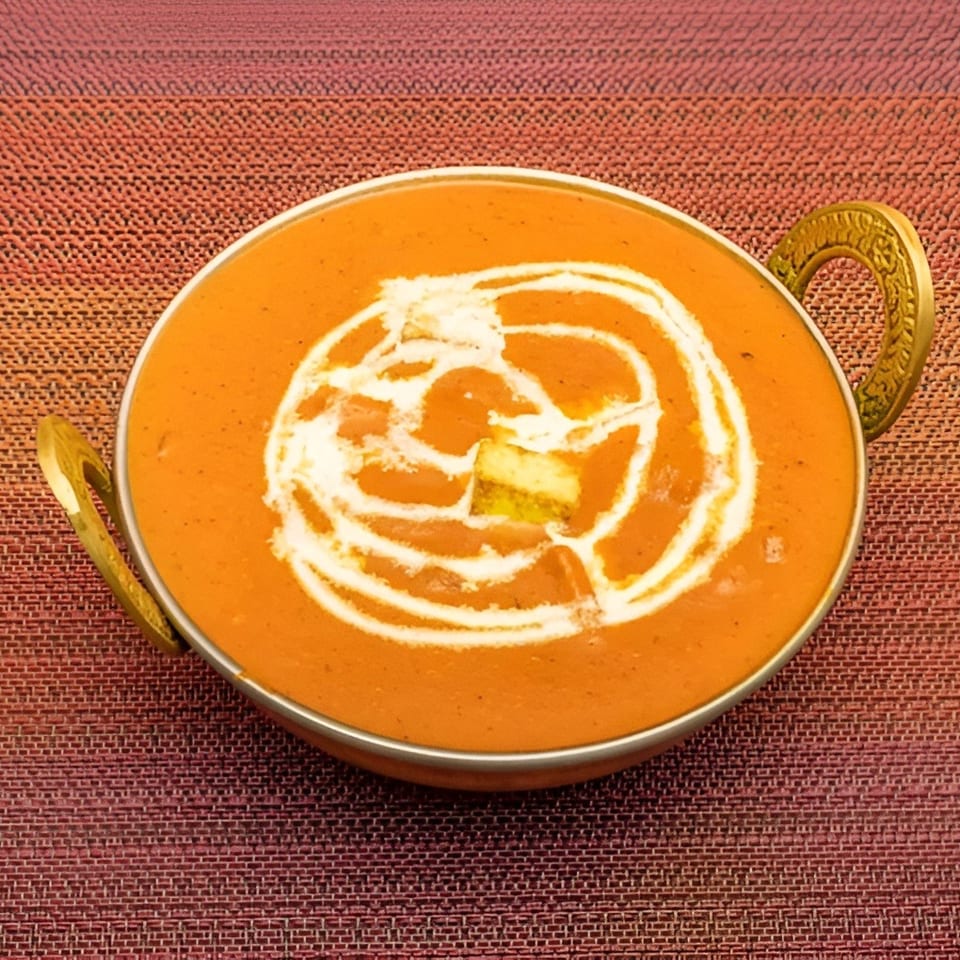 A golden bowl of creamy orange butter chicken, garnished with white cream swirls and paneer.