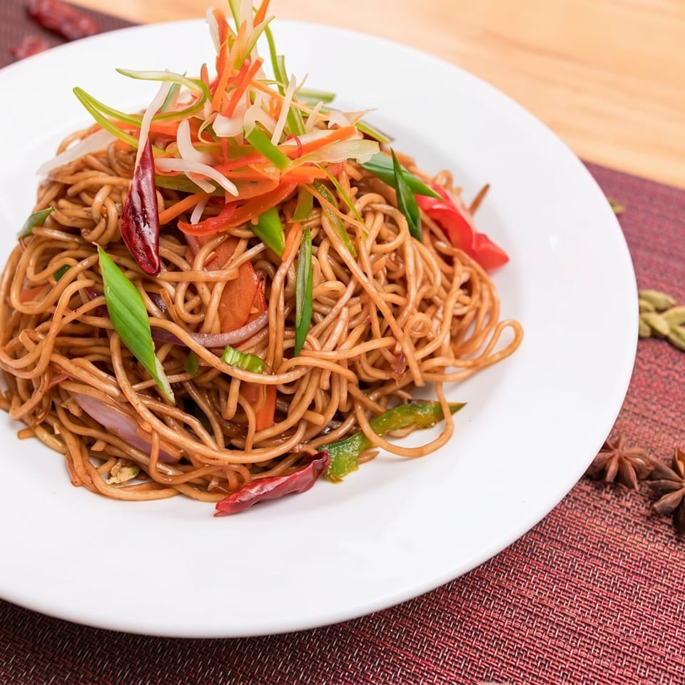 Noodles with colorful julienned vegetables and red chili peppers on a white plate.